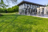 large patio in front of glass covered building with lawn area between it and trees outside