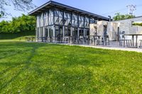 large patio in front of glass covered building with lawn area between it and trees outside