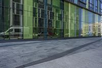 a fire hydrant stands by a large glass building in the foreground with a van and other vehicles reflected in windows