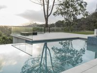 a glass enclosed swimming pool in front of a cityscape with a bench and tree