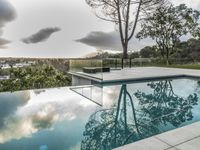 a glass enclosed swimming pool in front of a cityscape with a bench and tree