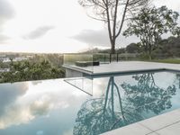 a glass enclosed swimming pool in front of a cityscape with a bench and tree