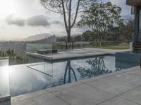 a glass enclosed swimming pool in front of a cityscape with a bench and tree