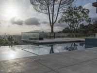 a glass enclosed swimming pool in front of a cityscape with a bench and tree