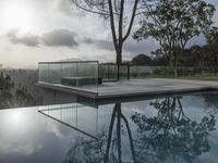 a glass enclosed swimming pool in front of a cityscape with a bench and tree