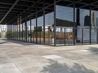 an empty walkway outside a glass building in the city with tables on the pavement and other architecture in the distance