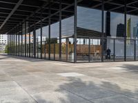 an empty walkway outside a glass building in the city with tables on the pavement and other architecture in the distance