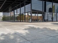 an empty walkway outside a glass building in the city with tables on the pavement and other architecture in the distance