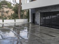 a glass garage is reflecting its surroundings on the wet ground outside with a white door and gray wall and windows