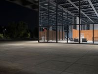 a room that has windows and chairs in it by some glass windows at night with some trees