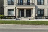 the house is gray with a black door and white trim and windows and a small green yard is next to the large building