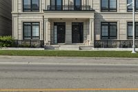 the house is gray with a black door and white trim and windows and a small green yard is next to the large building