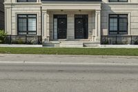 the house is gray with a black door and white trim and windows and a small green yard is next to the large building