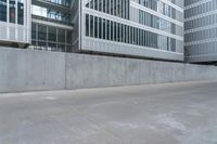 a woman riding a skateboard in an empty area next to buildings and a concrete wall