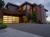 the garage door of a modern home opens up to the backyard deck with shrubs, grass and flowers