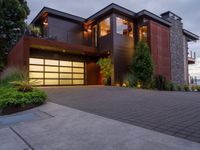 the garage door of a modern home opens up to the backyard deck with shrubs, grass and flowers