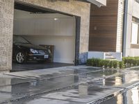 the driveway with stepping leading to a modern home with a car in the garage door and window, reflecting the rain and stone steps outside the concrete