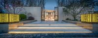 a modern home with some steps leading to it's entrance at night time on a cobblestone sidewalk and lawn area