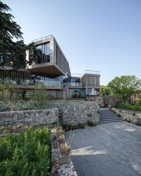 the exterior of a modern home surrounded by stones and trees a stairway leads to an open roof and the upper floor