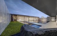 the courtyard of a modern home with glass walls and large rocks in the grass area