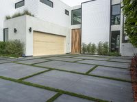 a modern home with concrete pavers and grass on it, there is a large garage