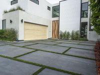 a modern home with concrete pavers and grass on it, there is a large garage