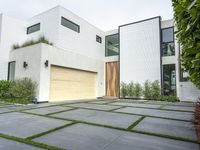 a modern home with concrete pavers and grass on it, there is a large garage