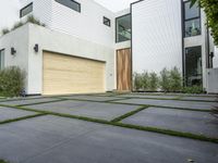 a modern home with concrete pavers and grass on it, there is a large garage