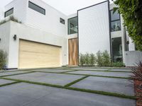 a modern home with concrete pavers and grass on it, there is a large garage