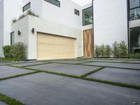 a modern home with concrete pavers and grass on it, there is a large garage