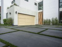 a modern home with concrete pavers and grass on it, there is a large garage