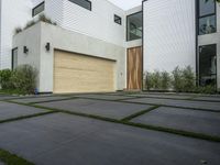 a modern home with concrete pavers and grass on it, there is a large garage