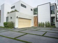 a modern home with concrete pavers and grass on it, there is a large garage