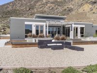 a modern home in an open field in front of a mountain view, with outdoor seating and a dining set