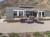 a modern home in an open field in front of a mountain view, with outdoor seating and a dining set