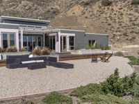 a modern home in an open field in front of a mountain view, with outdoor seating and a dining set