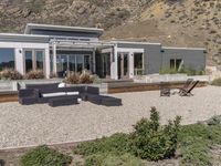 a modern home in an open field in front of a mountain view, with outdoor seating and a dining set