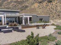 a modern home in an open field in front of a mountain view, with outdoor seating and a dining set