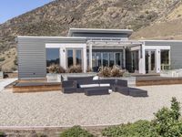 a modern home in an open field in front of a mountain view, with outdoor seating and a dining set