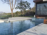 the large pool on the hillside overlooks the view of the valley below it and leads into a modern home's backyard