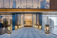 the entrance to a modern hotel with glass walls, pool, and pool side lamp