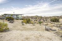 a small modern house sitting in the desert area of an abandoned park setting, next to a lone rock