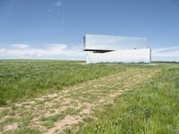 a modern house is sitting high above a hill of grass under a blue sky with white clouds