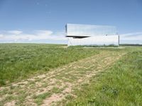 a modern house is sitting high above a hill of grass under a blue sky with white clouds