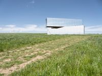 a modern house is sitting high above a hill of grass under a blue sky with white clouds