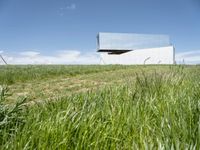 a modern house is sitting high above a hill of grass under a blue sky with white clouds