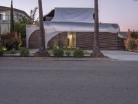 a house that is next to two palm trees with a white canopy attached to it