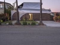 a house that is next to two palm trees with a white canopy attached to it