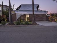 a house that is next to two palm trees with a white canopy attached to it