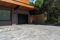 a modern house features paver stone with a wood ceiling over entrance and fenced in area